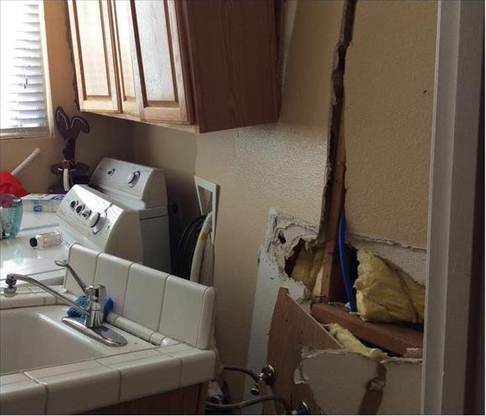 Laundry room wall showing considerable damage after a car crashed through it